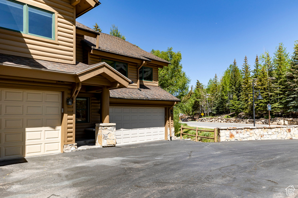 View of side of home with a garage, driveway, and roof with shingles