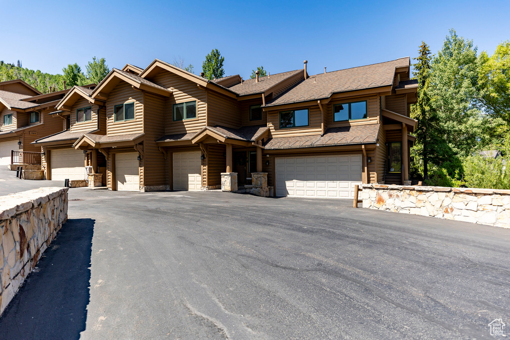 Townhome / multi-family property featuring a garage, stone siding, a shingled roof, and driveway