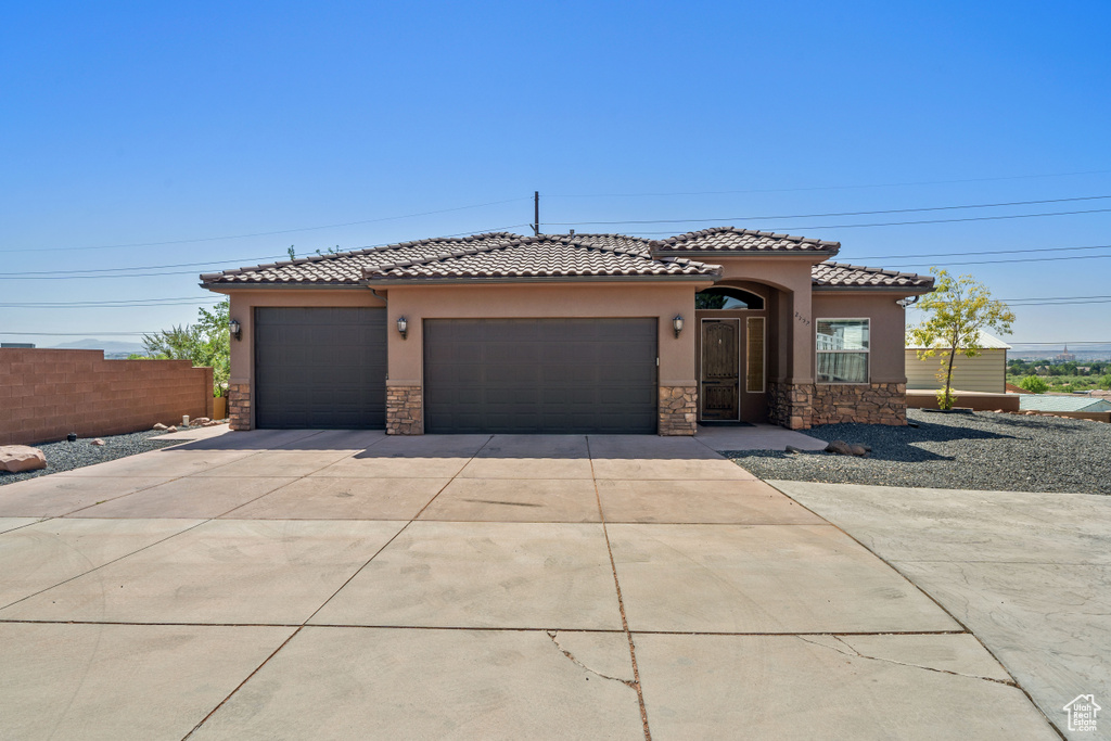 Mediterranean / spanish-style house featuring stone siding, stucco siding, a garage, concrete driveway, and a tile roof