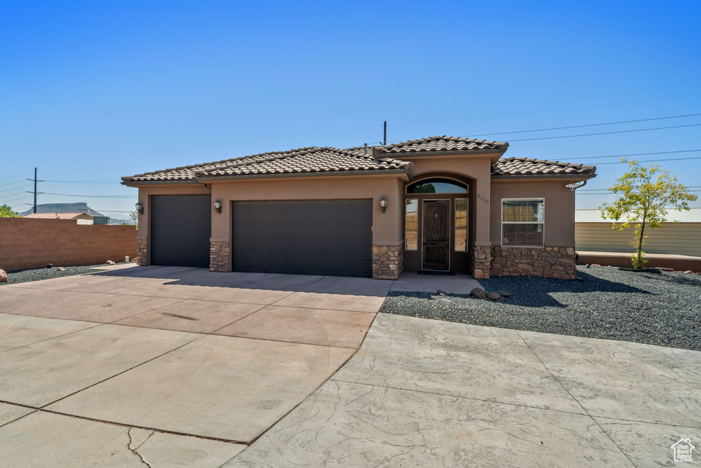 Mediterranean / spanish house featuring stone siding, stucco siding, driveway, an attached garage, and a tiled roof