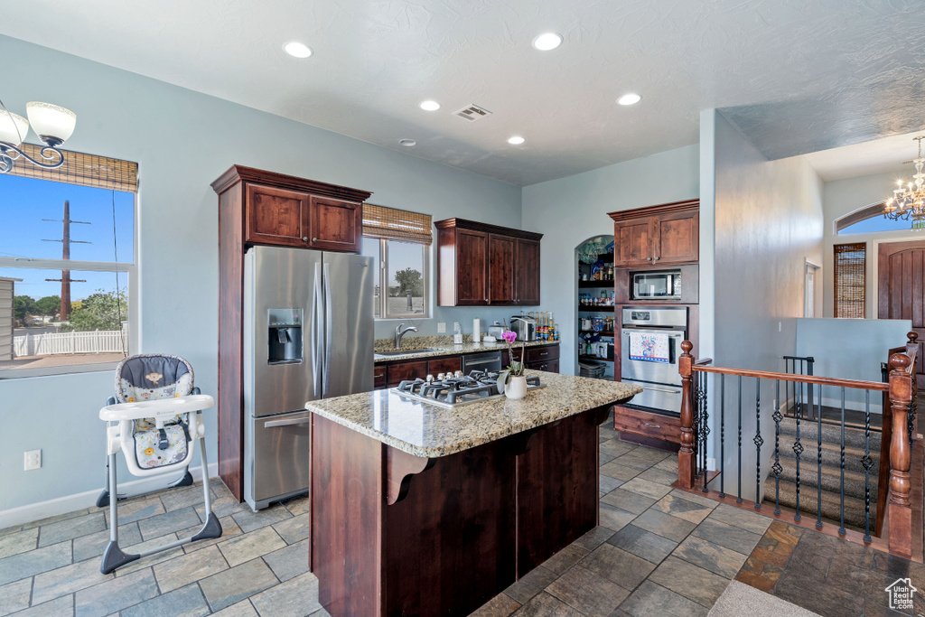 Kitchen with appliances with stainless steel finishes, a warming drawer, stone tile flooring, a chandelier, and a center island