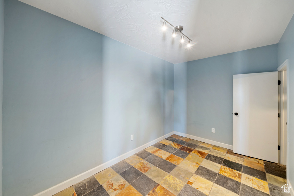 Empty room featuring stone tile flooring and rail lighting