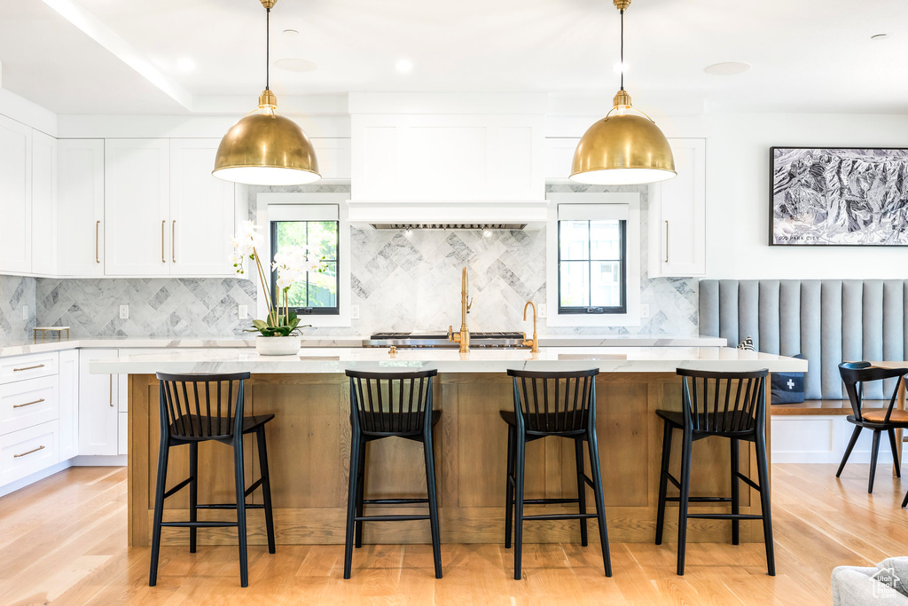 Kitchen featuring light wood finished floors, decorative backsplash, white cabinets, and an island with sink