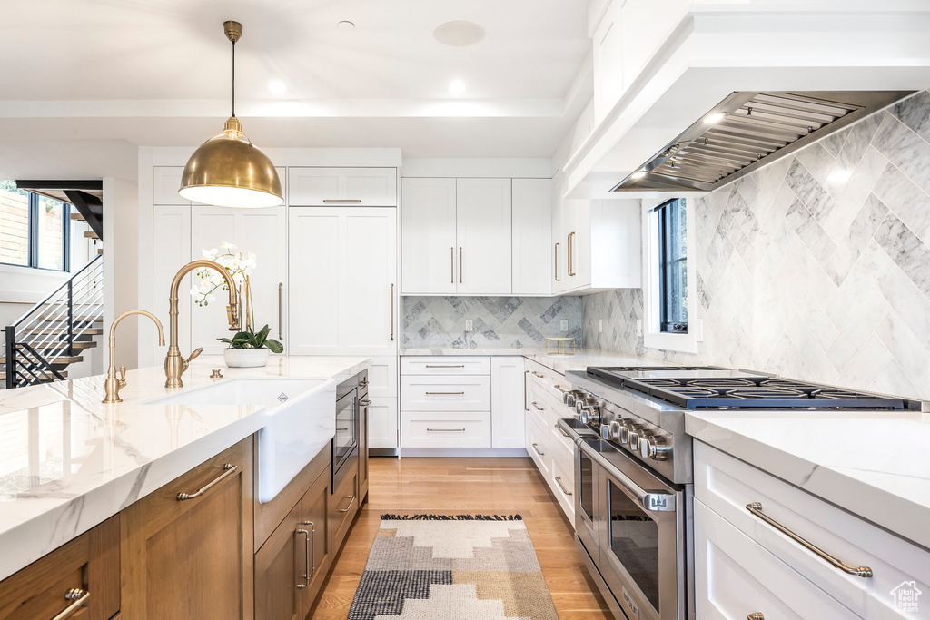 Kitchen featuring high end stove, light stone countertops, white cabinetry, premium range hood, and recessed lighting