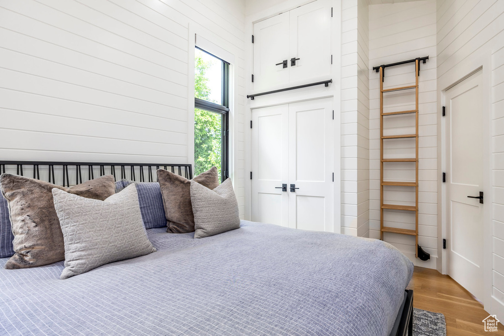 Bedroom with light wood finished floors, a closet, and wood walls