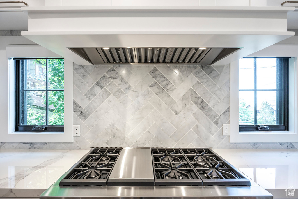Kitchen with range, backsplash, wall chimney range hood, and light stone countertops