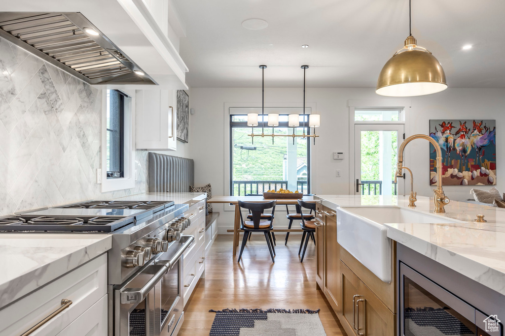 Kitchen with high end stainless steel range, wall chimney range hood, light stone countertops, backsplash, and wine cooler