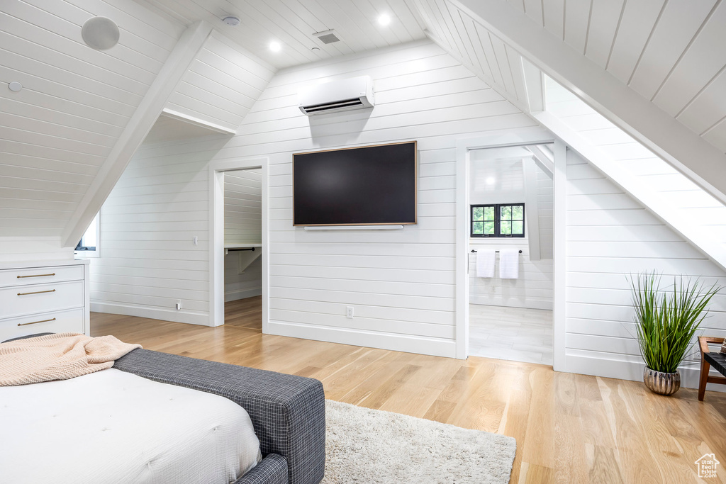 Bedroom with a wall mounted AC, lofted ceiling, light wood-style floors, wooden walls, and wood ceiling