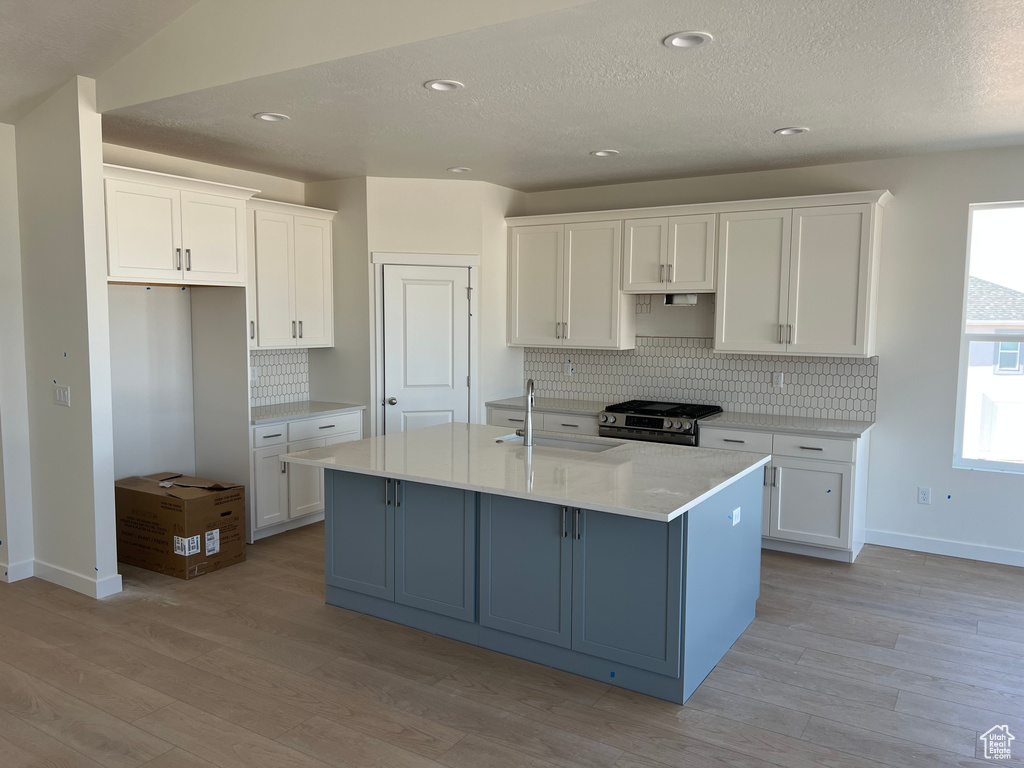 Kitchen featuring stainless steel gas range oven, tasteful backsplash, white cabinets, light wood-style floors, and recessed lighting