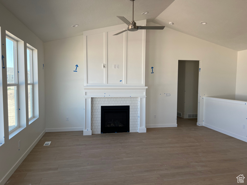 Unfurnished living room featuring a ceiling fan, vaulted ceiling, wood finished floors, a tile fireplace, and recessed lighting