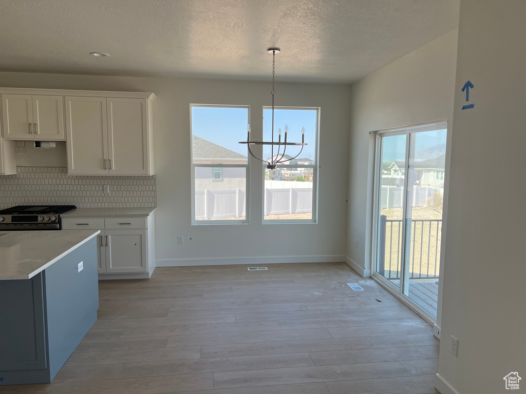 Kitchen with stainless steel gas range, light wood-type flooring, light countertops, white cabinets, and a chandelier