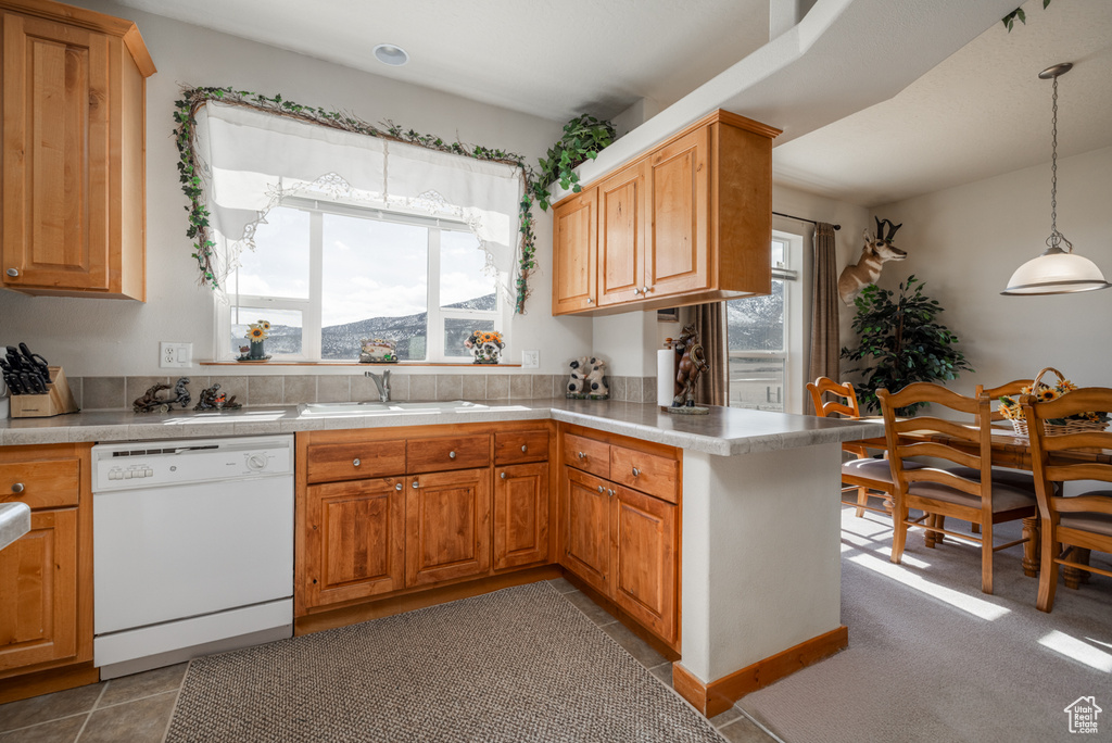Kitchen featuring white dishwasher, a peninsula, light countertops, hanging light fixtures, and tile patterned flooring