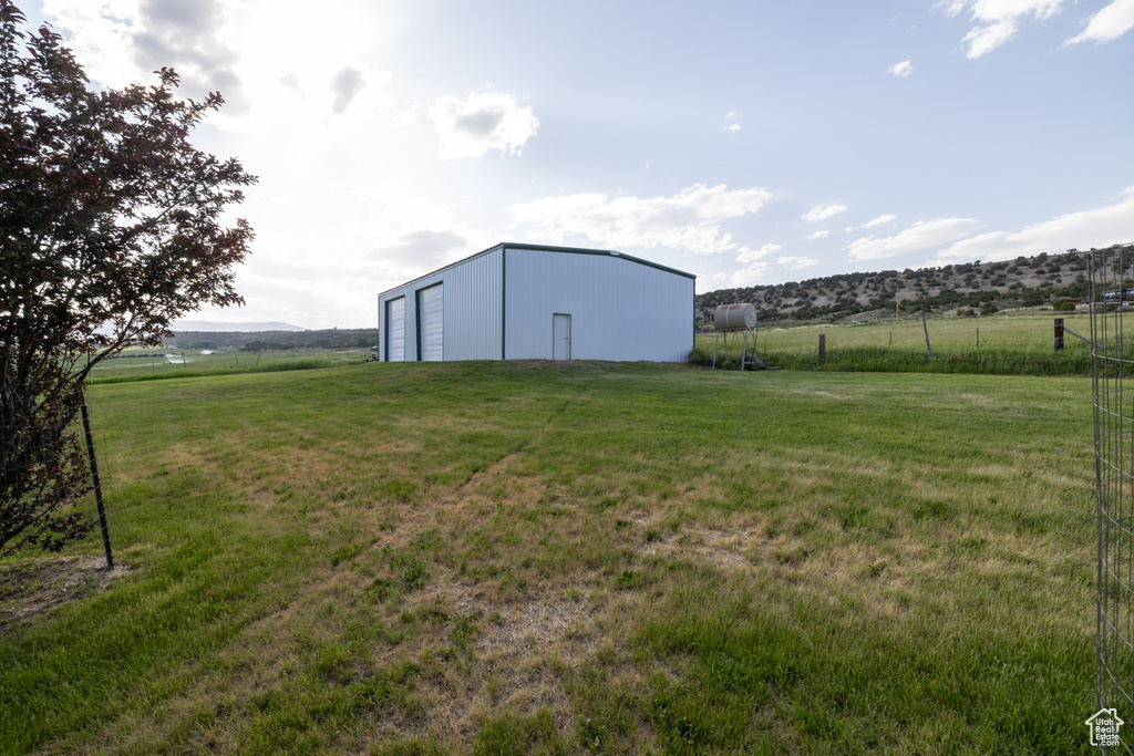 View of yard featuring a detached garage, a view of rural / pastoral area, an outdoor structure, and a pole building