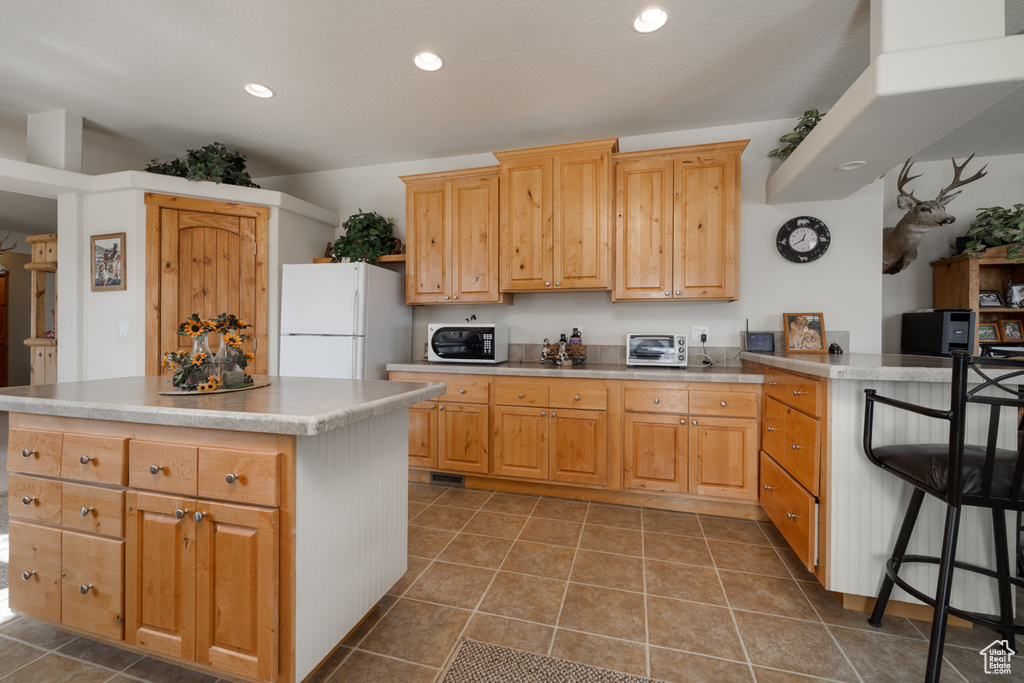 Kitchen with freestanding refrigerator, recessed lighting, a kitchen island, a peninsula, and tile patterned floors