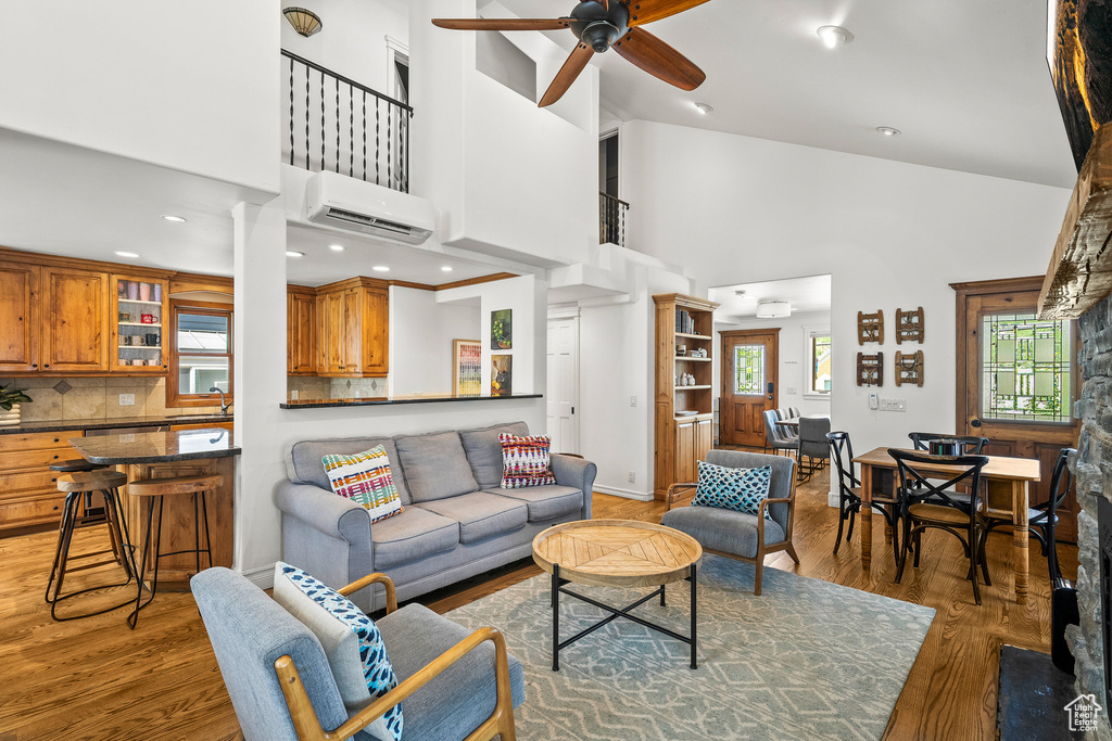 Living area featuring an AC wall unit, high vaulted ceiling, a ceiling fan, and light wood finished floors