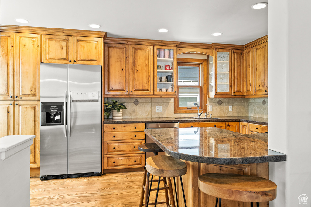 Kitchen featuring stainless steel appliances, a kitchen breakfast bar, light wood-style floors, recessed lighting, and glass insert cabinets
