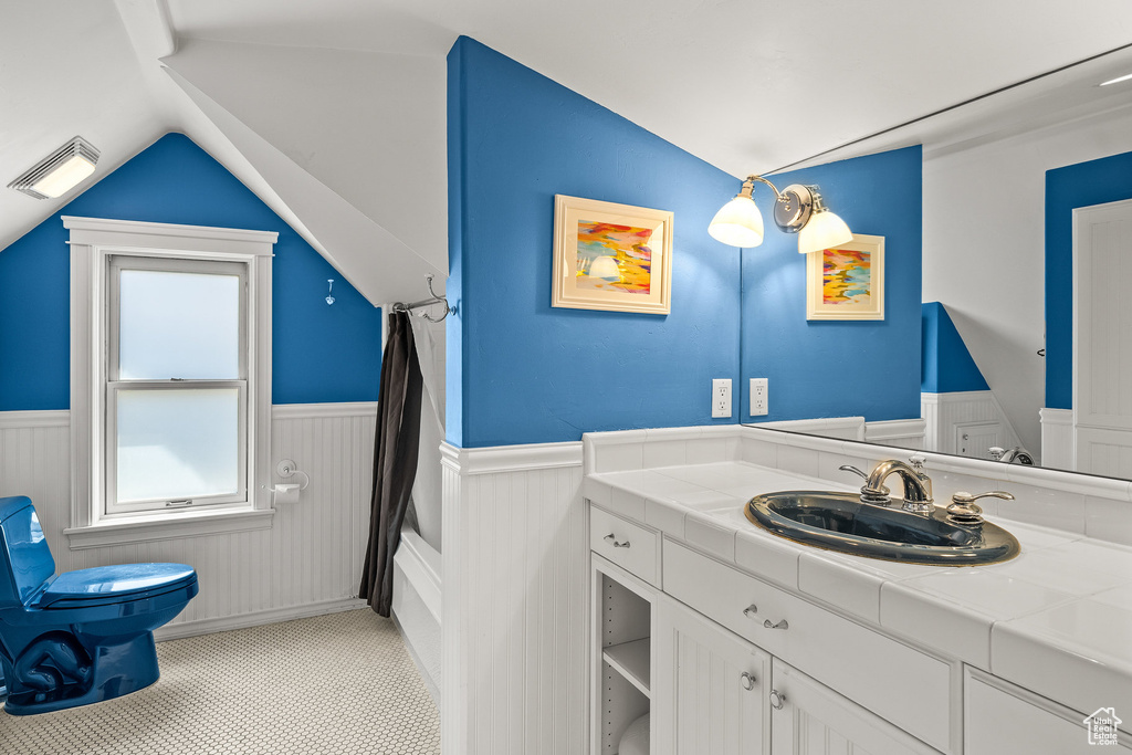 Bathroom with a wainscoted wall, vaulted ceiling, vanity, and shower / tub combo