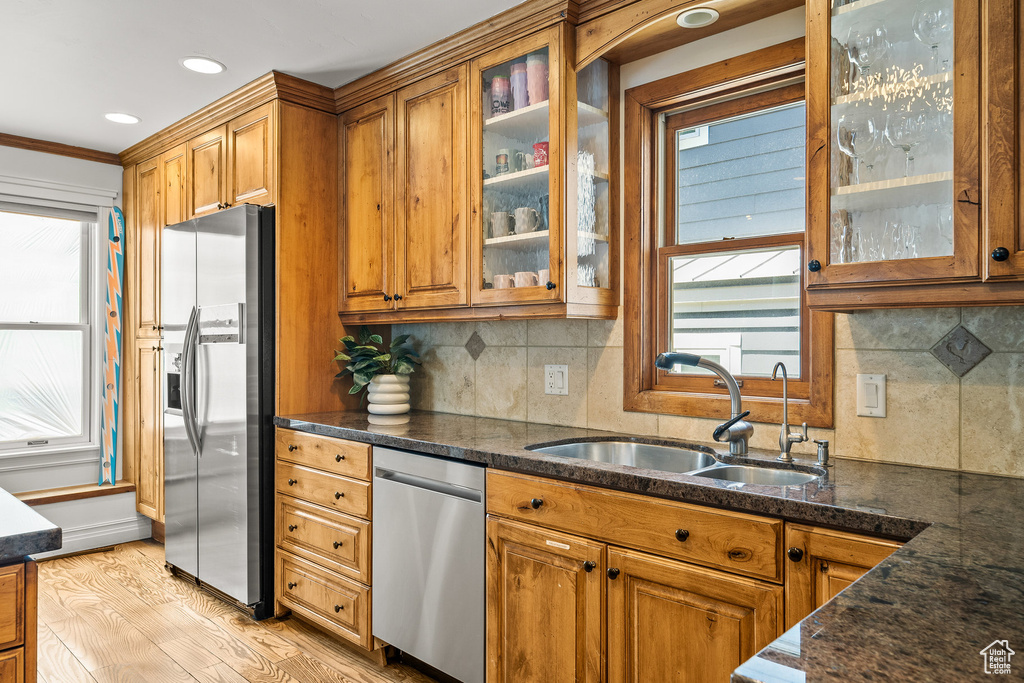 Kitchen with appliances with stainless steel finishes, brown cabinetry, light wood finished floors, decorative backsplash, and ornamental molding