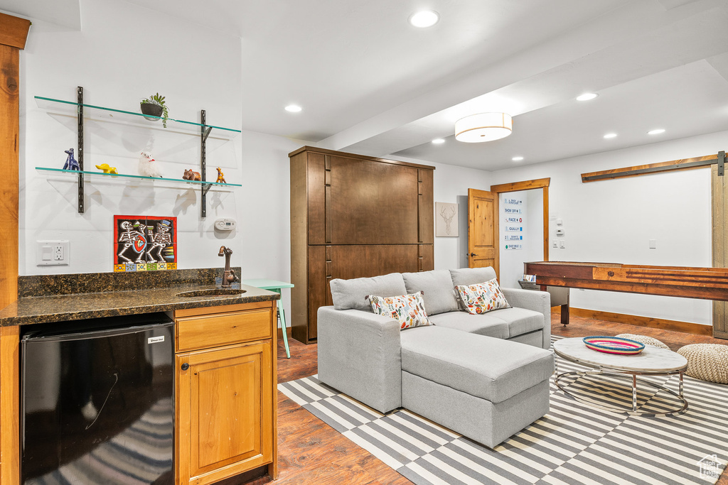 Living area with bar with sink, recessed lighting, wood finished floors, and a barn door