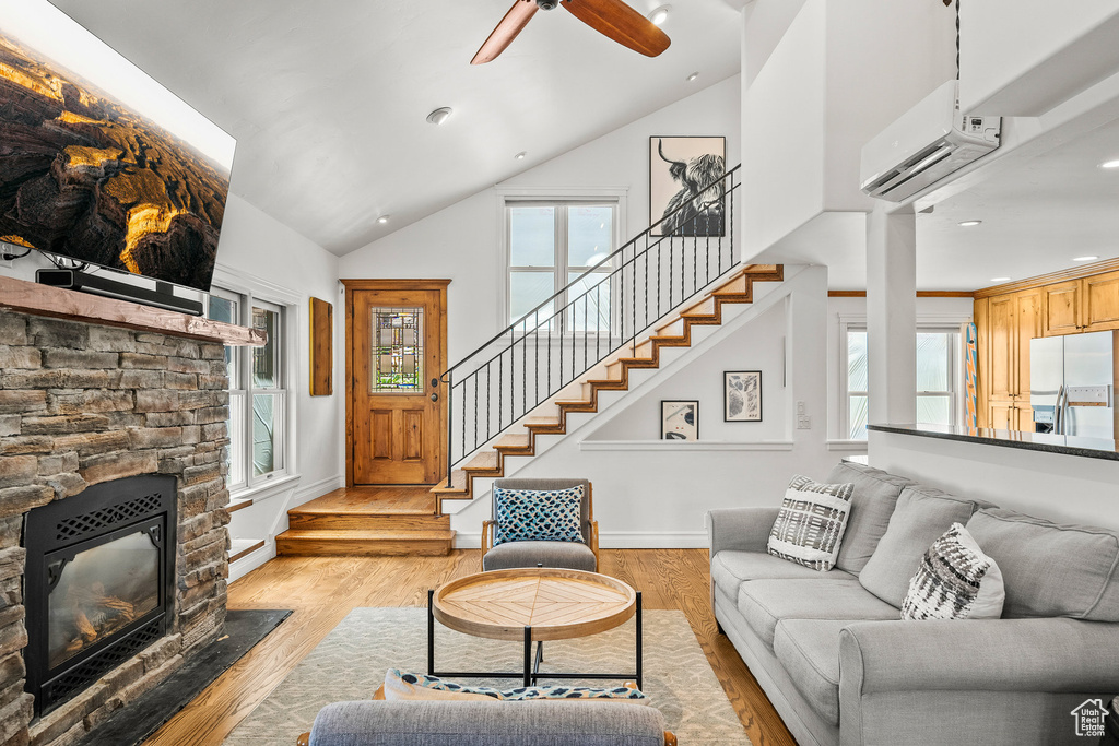 Living room with a wall mounted air conditioner, stairway, high vaulted ceiling, light wood finished floors, and healthy amount of natural light