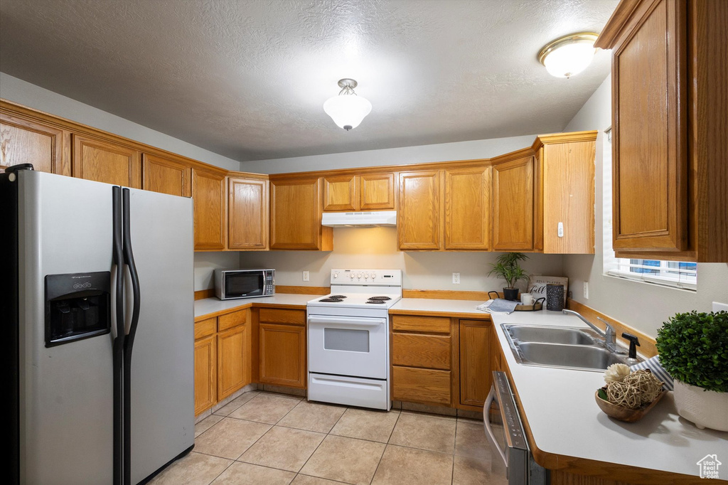 Kitchen featuring stainless steel appliances, under cabinet range hood, light countertops, brown cabinets, and a textured ceiling