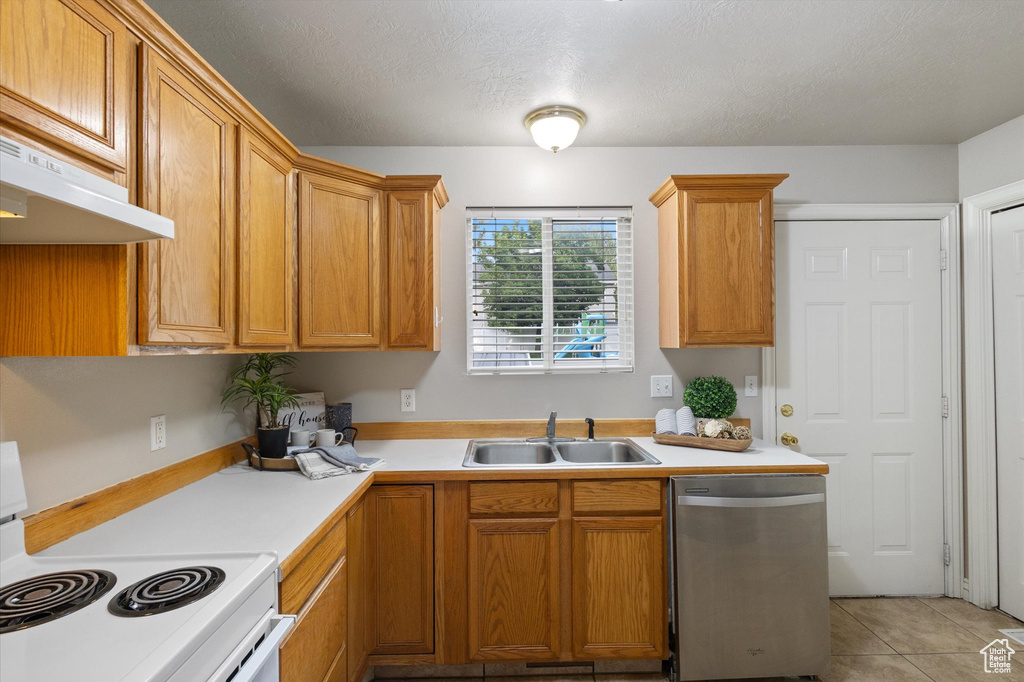 Kitchen featuring stainless steel dishwasher, white range with electric cooktop, light countertops, under cabinet range hood, and brown cabinets