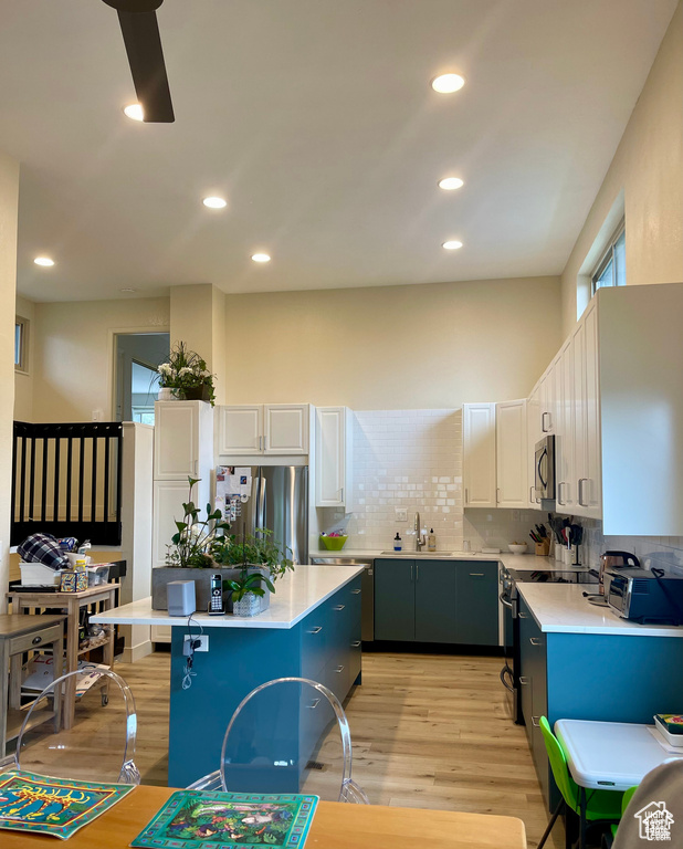 Kitchen with appliances with stainless steel finishes, light countertops, light wood-style flooring, backsplash, and a center island