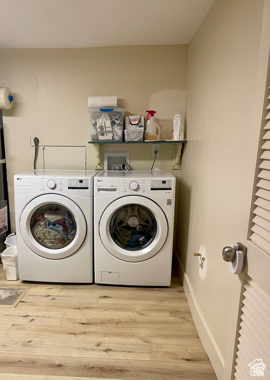 Washroom with washing machine and dryer and light wood-style flooring