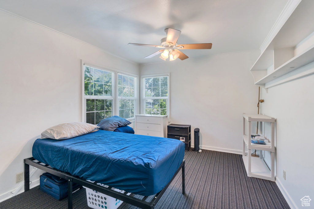 Bedroom with dark carpet, ornamental molding, and a ceiling fan