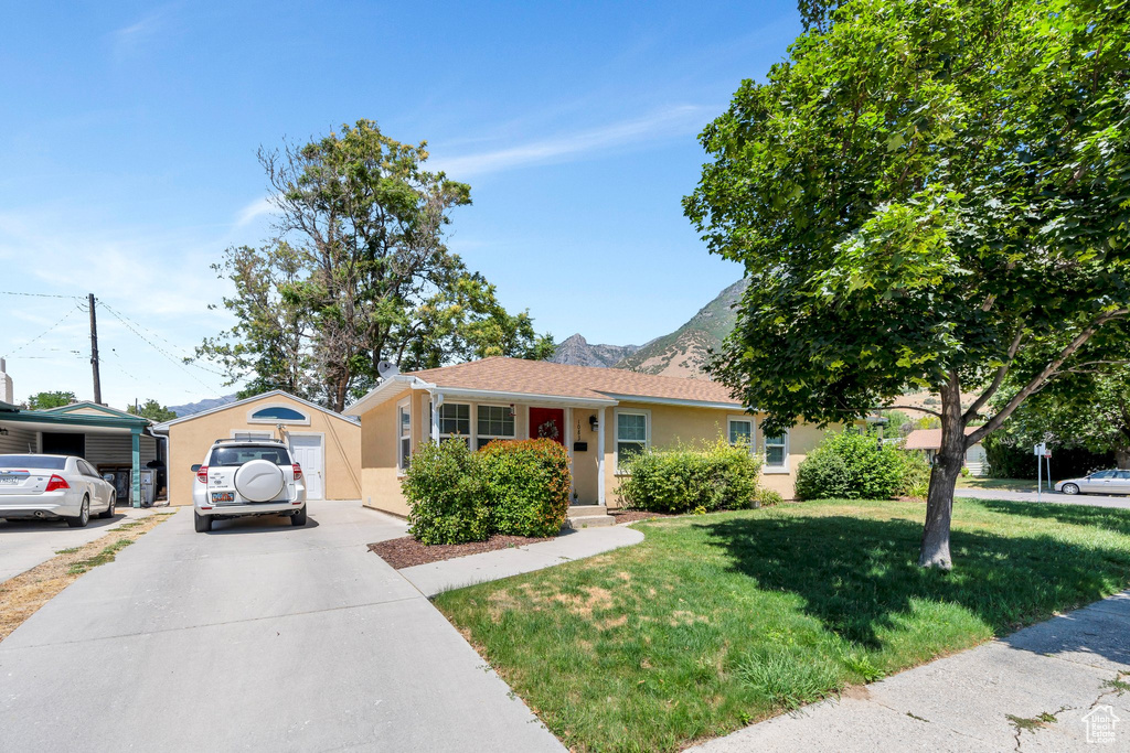 View of front facade featuring concrete driveway, stucco siding, a front lawn, and a mountain view