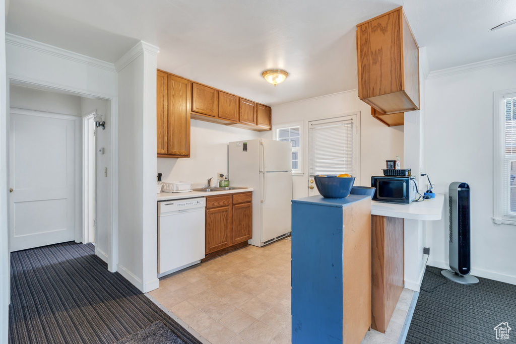 Kitchen featuring white appliances, light countertops, brown cabinets, plenty of natural light, and crown molding