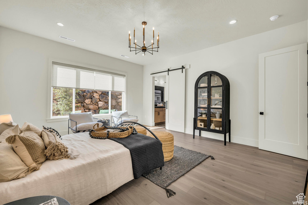 Bedroom featuring a barn door, light wood-style flooring, a chandelier, recessed lighting, and ensuite bath