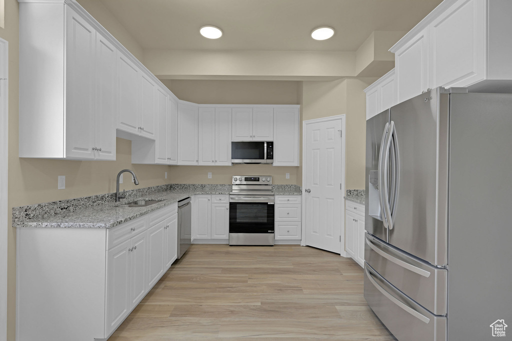 Kitchen featuring stainless steel appliances, white cabinetry, light stone countertops, and light wood-style flooring