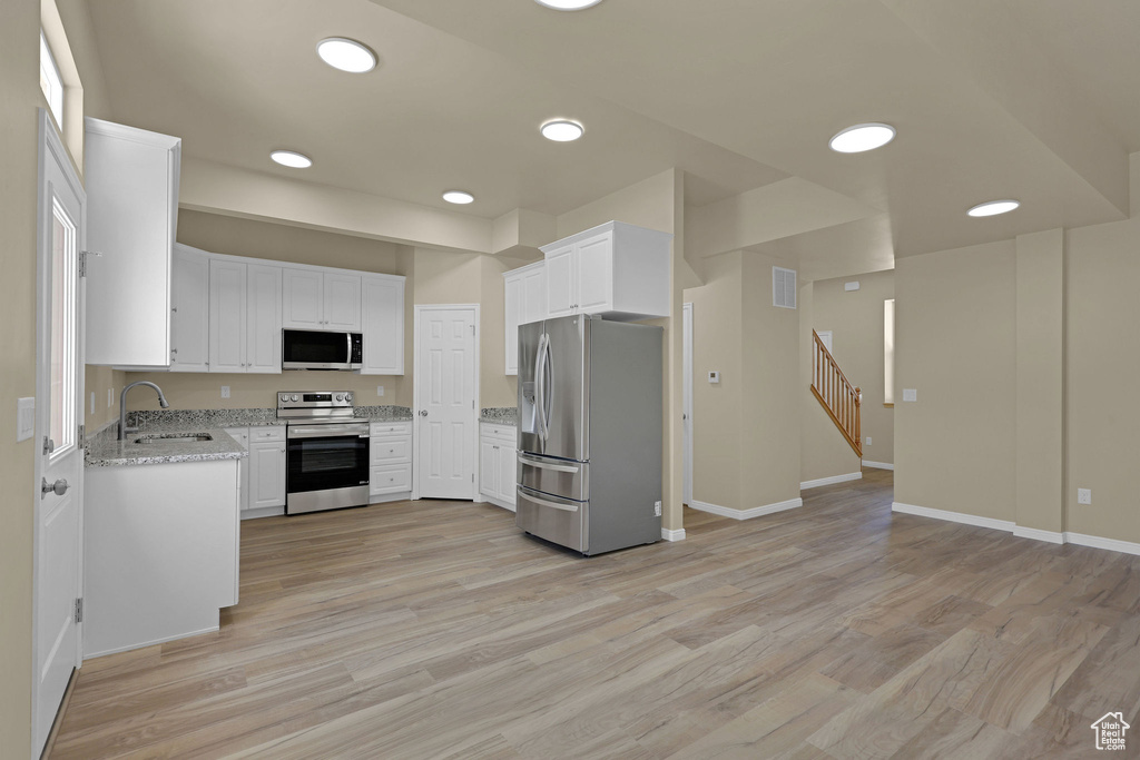 Kitchen featuring appliances with stainless steel finishes, light stone counters, white cabinetry, light wood-style flooring, and recessed lighting
