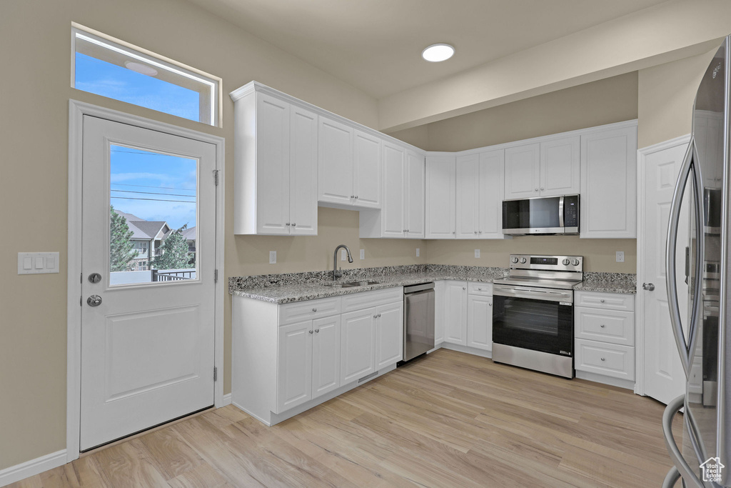 Kitchen with stainless steel appliances, light wood finished floors, white cabinetry, and light stone countertops