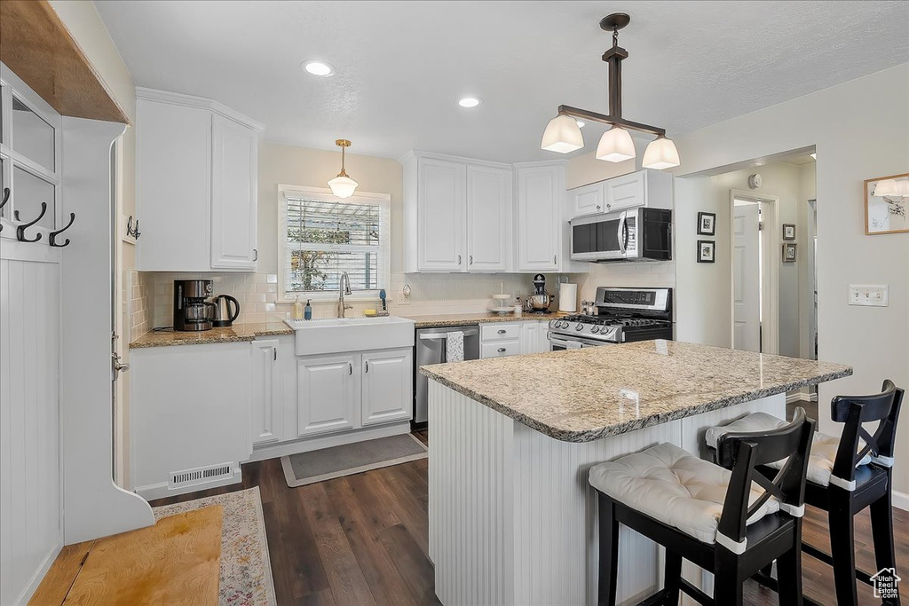 Kitchen featuring appliances with stainless steel finishes, dark wood finished floors, white cabinets, decorative backsplash, and a breakfast bar