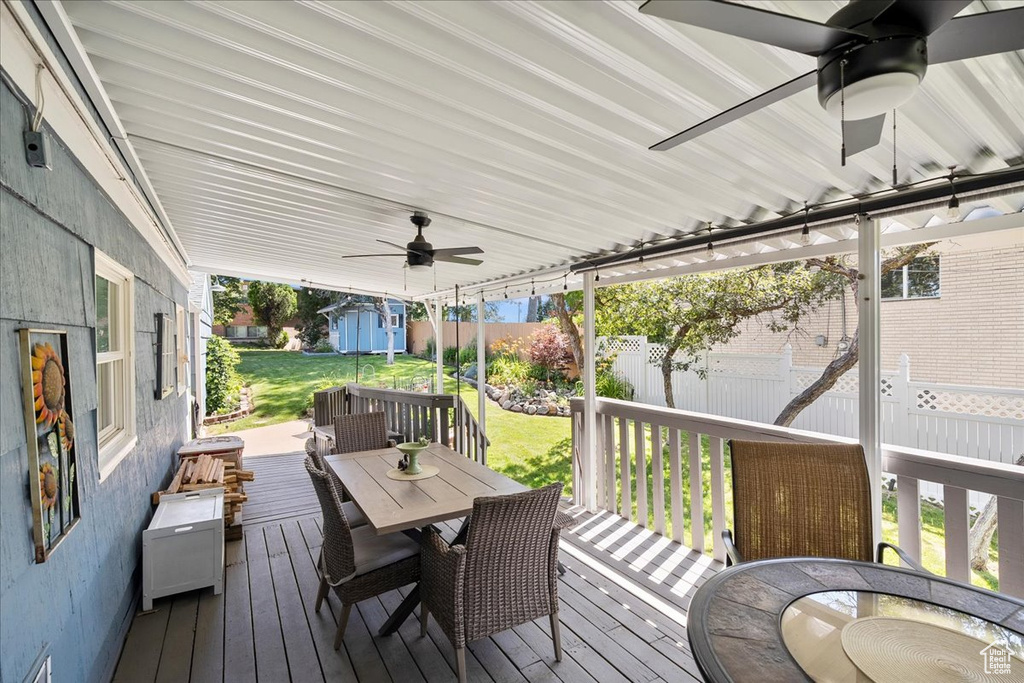 Wooden deck featuring outdoor dining space, a ceiling fan, and a storage shed