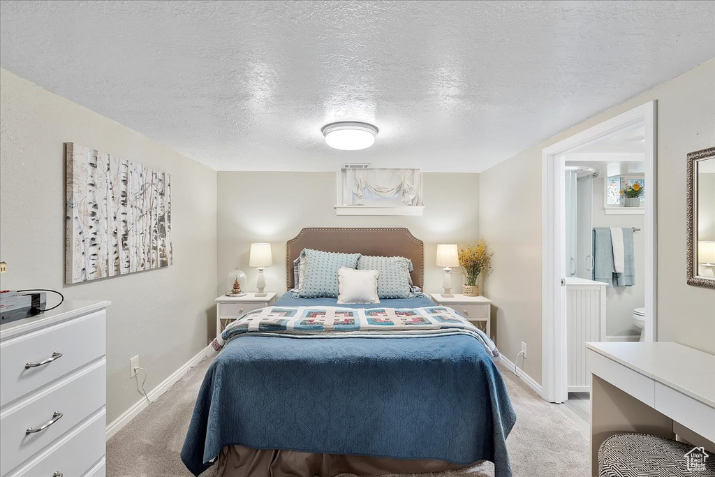 Bedroom with light carpet, a textured ceiling, and ensuite bath