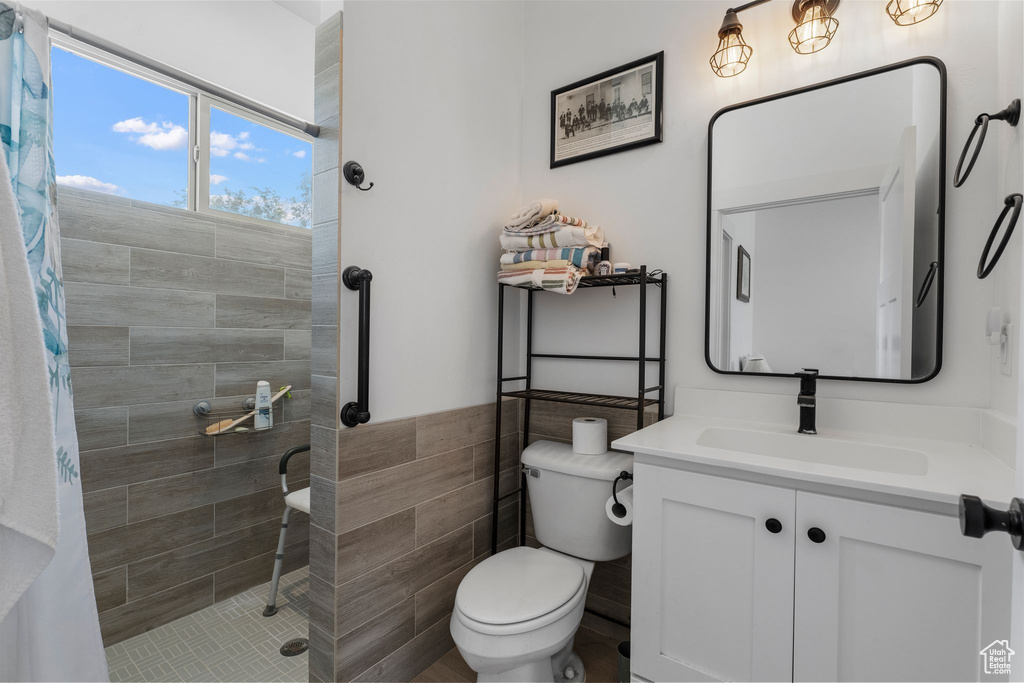 Full bathroom with a tile shower, vanity, and tile walls