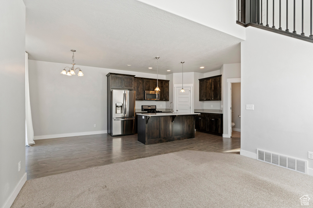 Kitchen with stainless steel appliances, open floor plan, dark colored carpet, a chandelier, and dark brown cabinetry