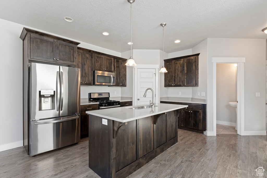 Kitchen with appliances with stainless steel finishes, dark brown cabinetry, wood finished floors, recessed lighting, and a textured ceiling