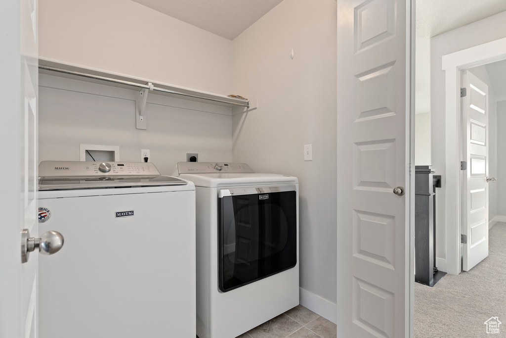 Washroom with washing machine and clothes dryer and light tile patterned floors