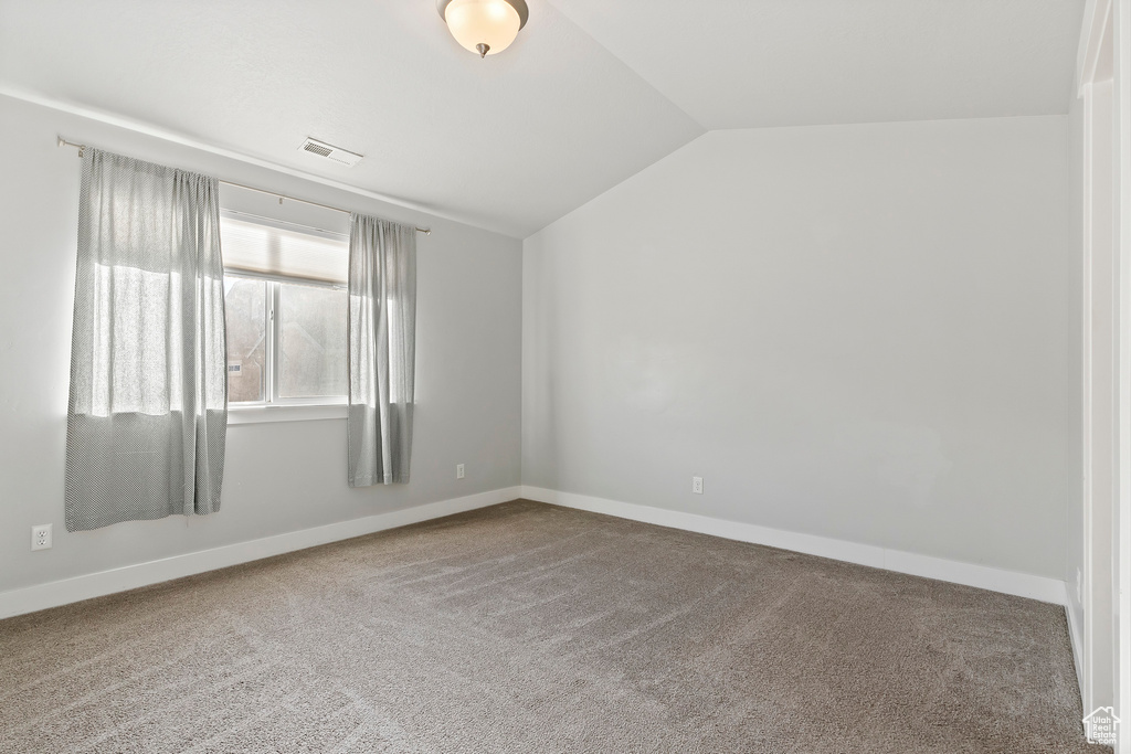 Carpeted spare room featuring lofted ceiling and baseboards