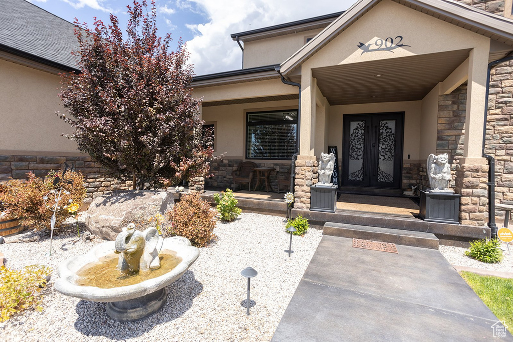 View of exterior entry featuring french doors, stone siding, stucco siding, and a porch
