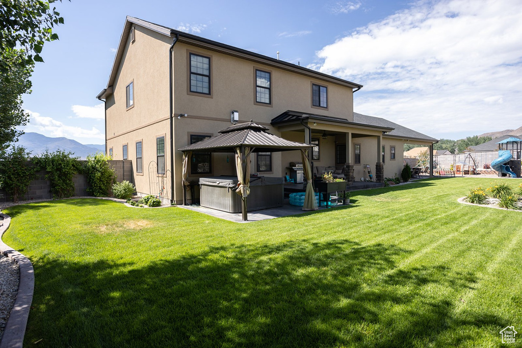 Rear view of house featuring a gazebo, a patio area, a fenced backyard, stucco siding, and a hot tub