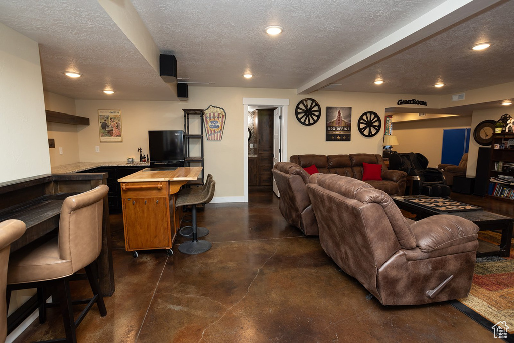Living area featuring finished concrete flooring, wet bar, a textured ceiling, recessed lighting, and beamed ceiling