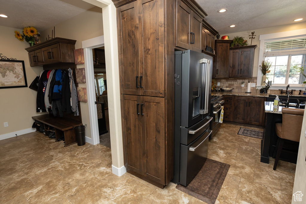 Kitchen with high quality fridge, light stone countertops, backsplash, dark brown cabinets, and recessed lighting