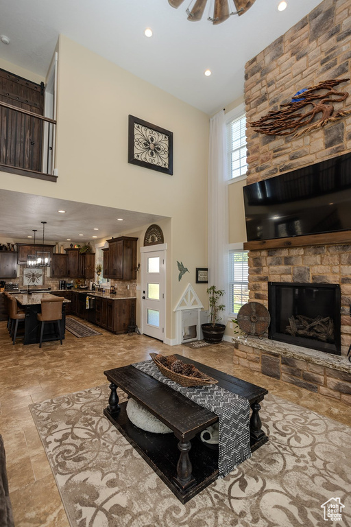 Living area with a high ceiling, recessed lighting, a stone fireplace, and light stone finish floors