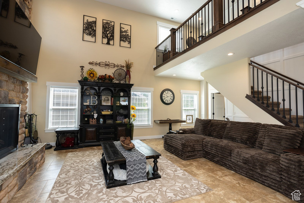 Living room with stairs, a stone fireplace, a high ceiling, and recessed lighting