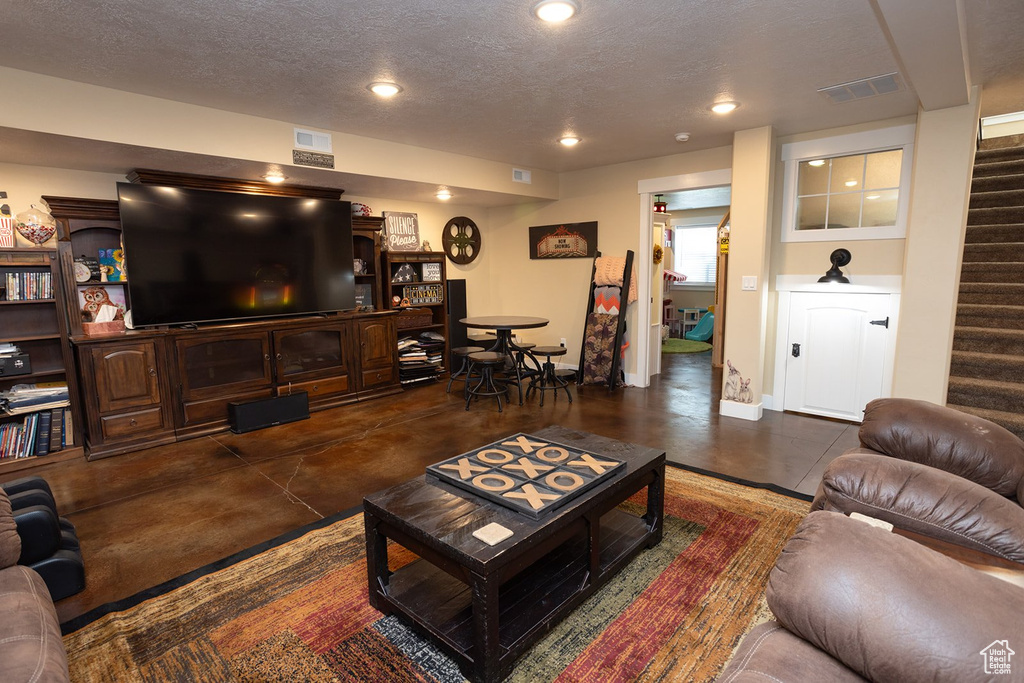 Living room with finished concrete floors, stairway, a textured ceiling, and recessed lighting
